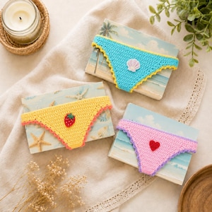 Puede incluir: Tres braguitas de bikini de ganchillo en azul brillante, amarillo y rosa. La braguita azul presenta una aplicación de concha blanca, la amarilla tiene una aplicación de fresa roja y la rosa muestra una aplicación de corazón rojo.
