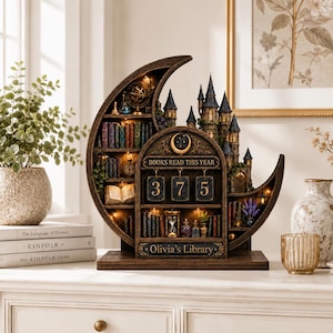 May include: A crescent moon-shaped wooden bookshelf display featuring a miniature castle, shelves filled with books, an hourglass, and a mechanical counter displaying the text BOOKS READ THIS YEAR and the name Olivia's Library with the number 375.