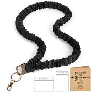May include: Black lanyard with a textured, gathered fabric design. It features a bronze-colored clasp and key ring. Includes two clear plastic badge holders and a card with the text "Never forget the difference that you make" and a rainbow.
