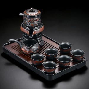 Può includere: Servizio da tè nero e color rame su un vassoio di legno. Il set comprende una teiera, una brocca e sei tazzine. La teiera presenta un motivo a drago. Il vassoio è in legno.