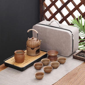 May include: A brown ceramic tea set with a teapot, warming stand, serving pitcher, and small cups. The set includes a grey carry case and a bamboo tray. The teapot has a woven handle. The set is designed for tea.