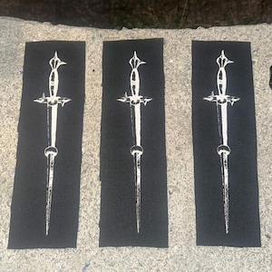 May include: Three rectangular black fabric patches, each featuring a centered white screen-printed graphic of a sharp, pointed dagger. The daggers have detailed hilts, crossguards, and long, slender blades, presented in a vertical orientation.