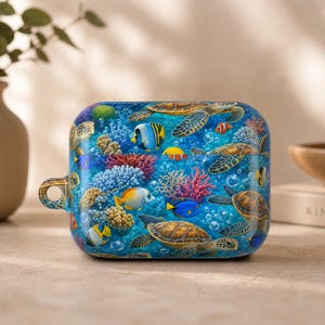 May include: A rectangular protective case for wireless earbuds featuring a vibrant underwater scene. The design displays multiple sea turtles swimming among colorful coral reefs, various tropical fish, and small bubbles on a deep blue background.