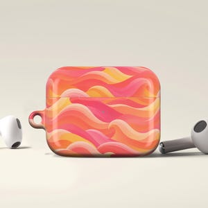 May include: A protective case for wireless earbuds featuring a vibrant, wavy pattern in shades of coral, pink, and yellow. The rectangular case has a small side loop and is positioned between two white wireless earbuds on a neutral background.