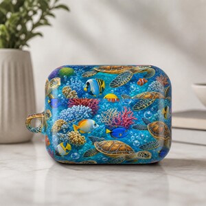 May include: A rectangular protective case for wireless earbuds featuring a vibrant underwater scene. The design displays multiple sea turtles swimming among colorful coral reefs, various tropical fish, and bubbles against a deep blue ocean background.