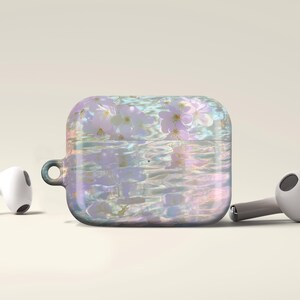 May include: A square, iridescent case for wireless earbuds, adorned with a floral design. The case is accompanied by two white and gray earbuds. The case features a pearlescent finish with a floral pattern, creating a dreamy aesthetic.