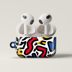 May include: White wireless earbuds rest on a case with a vibrant abstract design. The case features a black, white, red, yellow, and blue pattern. The case has a small blue loop on the side.