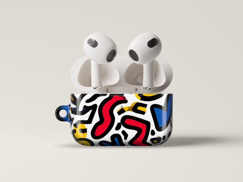 May include: White wireless earbuds rest on a case with a vibrant abstract design. The case features a black, white, red, yellow, and blue pattern. The case has a small blue loop on the side.