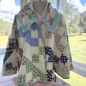 May include: A quilted jacket constructed from various fabric patches featuring a mix of patterns including blue and white polka dots, green and yellow geometric shapes, plaid, and floral prints. The jacket has a wide collar and long sleeves.