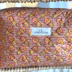 May include: A quilted cosmetic bag with a floral pattern in shades of pink, yellow, and brown. The bag features a repeating design of flowers and leaves. The word "watercue" is printed on a white label. The bag is rectangular and has a zipper closure.