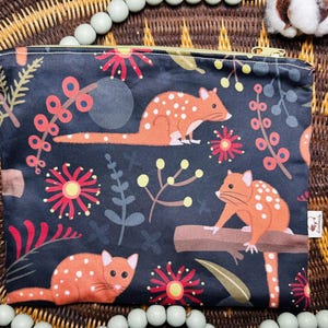 May include: A rectangular, dark blue pouch with a zipper closure. The pouch features a repeating pattern of orange animals with white spots, red flowers, and green foliage. The zipper is gold.