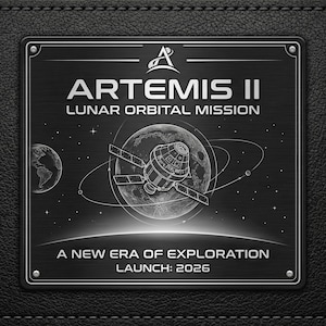 May include: A black metal plaque with the text "ARTEMIS II LUNAR ORBITAL MISSION" and a detailed illustration of a spacecraft orbiting the moon. The plaque also includes the text "A NEW ERA OF EXPLORATION LAUNCH: 2026".