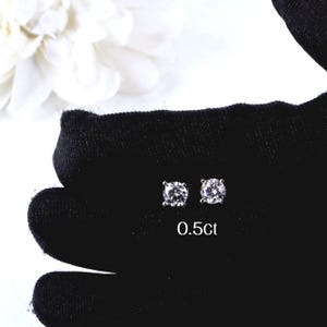 May include: A pair of sparkling diamond stud earrings, each with a round, brilliant-cut stone. The earrings are set against a black background, with the text "0.5ct" visible. The image showcases the earrings' clarity and brilliance.