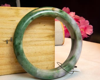 Op de afbeelding: Een jade armband met groene en lavendelkleurige tinten. Het gepolijste oppervlak van de armband reflecteert licht en toont de natuurlijke kleurvariaties. De cirkelvormige armband is een sieraad.