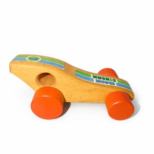 Puede incluir: Coche de carreras de juguete de madera con ruedas naranjas y carrocería de madera natural. El coche presenta rayas azules y verdes y el texto "MEAN STREAK". Un juguete clásico para niños.