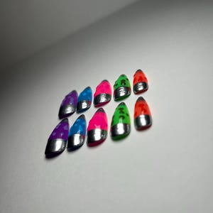 May include: Ten brightly coloured nail tips are displayed. Each tip features a silver base and a glossy top in shades of purple, blue, pink, green, and red. The tips are arranged in two rows, showcasing their varied hues.