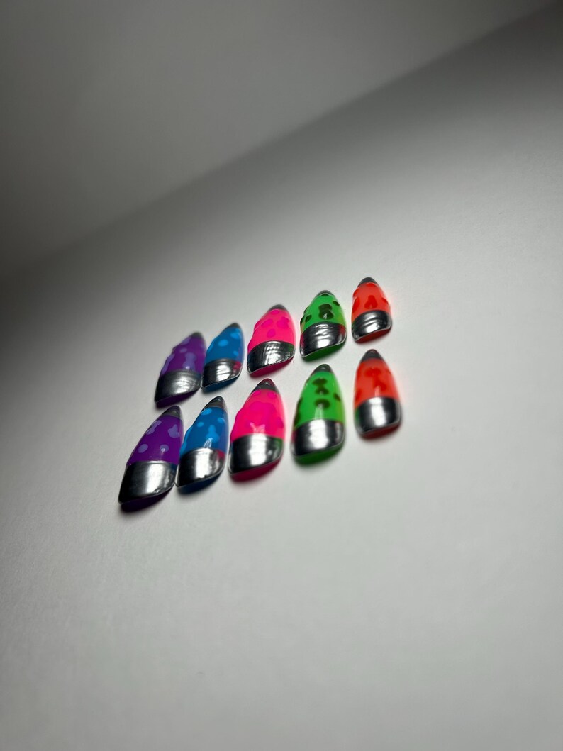 May include: Ten brightly coloured nail tips are displayed. Each tip features a silver base and a glossy top in shades of purple, blue, pink, green, and red. The tips are arranged in two rows, showcasing their varied hues.