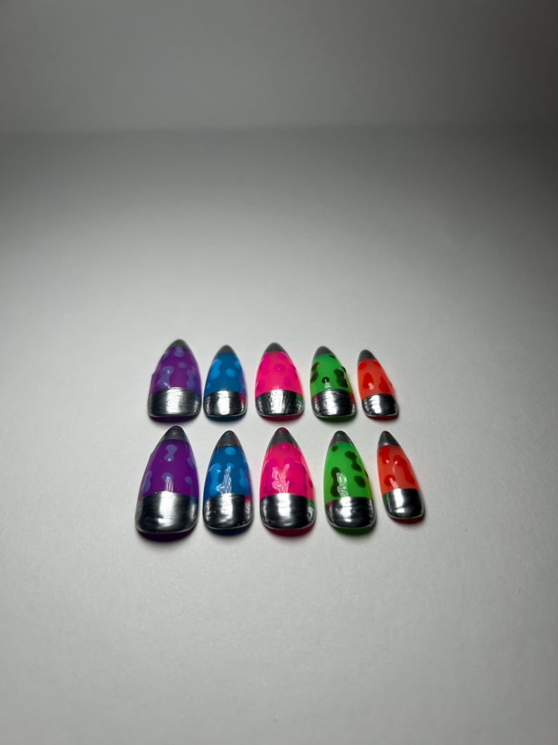 May include: A collection of ten brightly coloured false nails. Each nail has a silver base and a vivid top in shades of purple, blue, pink, green, and red. The nails are decorated with various patterns and designs.