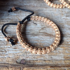 May include: A brown and white braided bracelet with a black cord closure. The bracelet is made of natural materials and has a rustic look.
