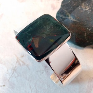 May include: A silver cuff bracelet with a square green and red gemstone set in the center.