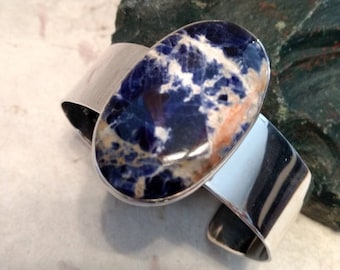 May include: A silver cuff bracelet with a large oval blue and white gemstone set in the center.