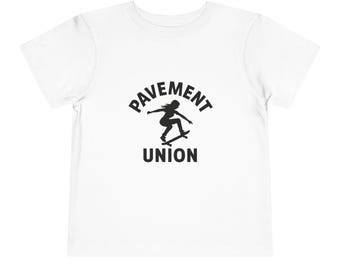 Może przedstawiać: Biała koszulka dla malucha z czarną grafiką. Grafika przedstawia słowa "PAVEMENT UNION" w okrągłym wzorze, z sylwetką osoby jeżdżącej na deskorolce pośrodku.