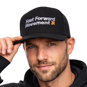 Puede incluir: Gorra de b&eacute;isbol negra con el texto bordado "Fast Forward Movement" en blanco y naranja. La gorra tiene una visera curva y la sostiene una persona.