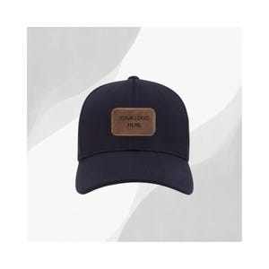 May include: Navy blue baseball cap with a curved brim. A rectangular, brown leather patch is centered on the front, displaying the text "YOUR LOGO HERE". The cap is a classic style, suitable for various activities.