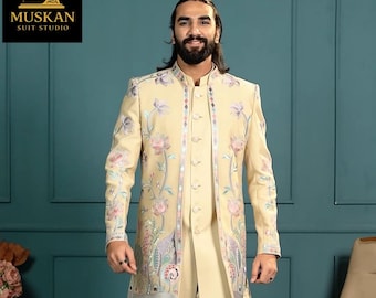 May include: A cream-coloured suit with floral embroidery. The suit includes a long jacket, a button-down shirt, and matching trousers. The jacket features intricate floral designs in pink, purple, and green. The Muskan Suit Studio logo is in the top left corner.