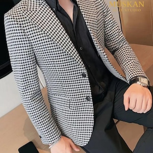 May include: A black and white houndstooth blazer with a two-button closure. The blazer is paired with a black shirt and black pants. The image also shows a watch and a smartphone.