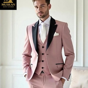 May include: A three-piece suit in a dusty rose color with black lapels and trim. The suit includes a jacket, vest, and trousers. A white dress shirt and tie are worn underneath. The logo for Muskan Suit Studio is in the upper left corner.