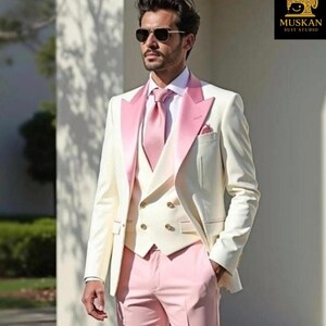May include: A cream-colored suit with a pink lapel, tie, and trousers. The suit includes a three-piece vest and a pocket square. The image also shows sunglasses and the text "MUSKAN SUIT STUDIO".