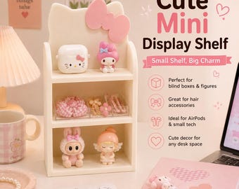 May include: A cream-coloured mini display shelf shaped like a cat head with a large pink bow. The shelf has three tiers holding small figurines, an AirPods case, and hair accessories. Text on the right reads Cute Mini Display Shelf and Small Shelf, Big Charm.