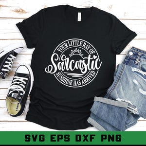 Puede incluir: Camiseta negra con el texto "Your Little Ray of Sarcastic Sunshine Has Arrived" en un dise&ntilde;o circular blanco. La camiseta se combina con zapatillas blancas y negras y vaqueros azules doblados.