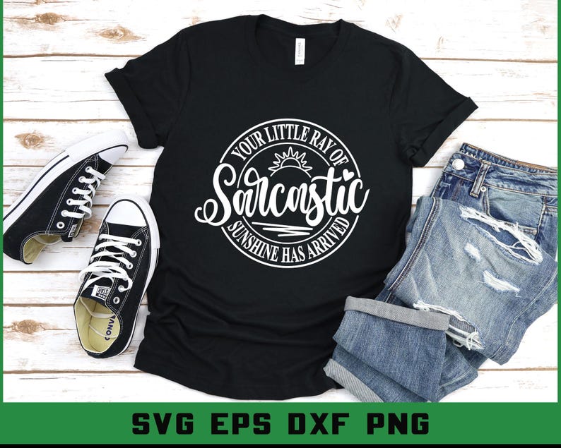 Puede incluir: Camiseta negra con el texto "Your Little Ray of Sarcastic Sunshine Has Arrived" en un dise&ntilde;o circular blanco. La camiseta se combina con zapatillas blancas y negras y vaqueros azules doblados.