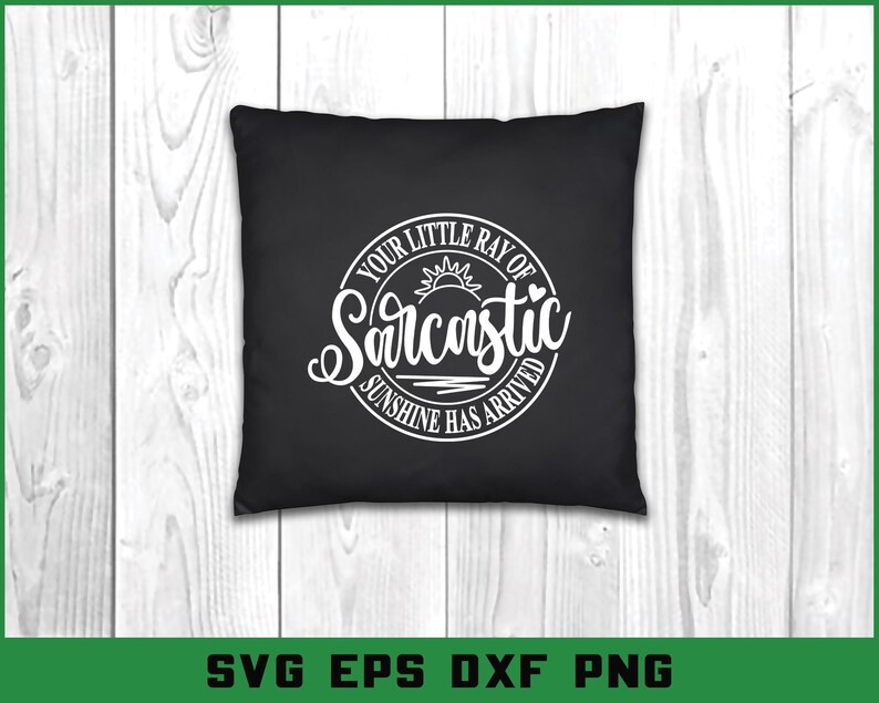 Puede incluir: Coj&iacute;n cuadrado negro con texto blanco que dice "YOUR LITTLE RAY OF Sarcastic SUNSHINE HAS ARRIVED" en un dise&ntilde;o circular. El dise&ntilde;o incluye un sol y un coraz&oacute;n. El coj&iacute;n est&aacute; sobre una superficie de madera clara.