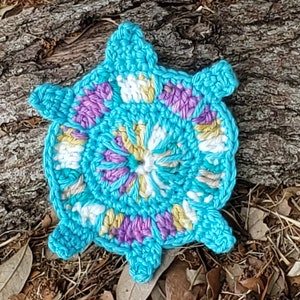May include: A crocheted turquoise coaster with a colorful floral design in shades of pink, yellow, and white.