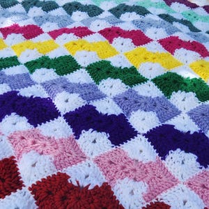 May include: A colorful crochet blanket with a chevron pattern. The blanket is made with different shades of red, pink, purple, blue, green, yellow, and white yarn.