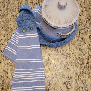 May include: Blue and white striped kitchen towel with a crocheted potholder attached. The towel has white stripes and a blue background. The potholder is blue and has two brown buttons.