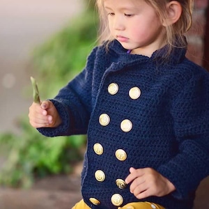 May include: A navy blue double-breasted crochet jacket featuring long sleeves, a collared neckline, and eight round, metallic gold-toned buttons arranged in two vertical rows down the front of the garment, creating a classic nautical-inspired look.