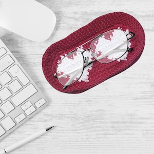 May include: A red woven heart-shaped glasses holder with a pair of glasses resting inside.