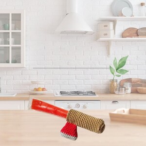 May include: A red ice pop in a clear plastic wrapper, with a crocheted cozy. The cozy is tan with a red and white striped accent. The item is on a wooden surface in a kitchen setting.