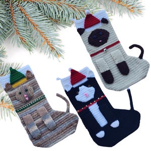 May include: Three handmade crochet Christmas stockings in the shape of cats. Each stocking features a cat face and body, with a Santa hat. The stockings are in shades of beige, brown, and black, with white and red accents. A festive holiday decoration.