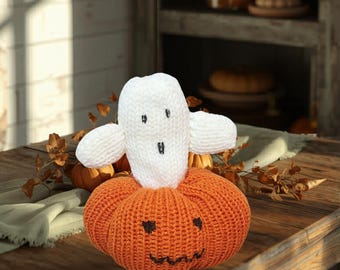 May include: A crocheted decoration featuring a bright orange pumpkin base with a stitched black jack-o'-lantern face and a white ghost figure with a stitched black face resting on top of the pumpkin.