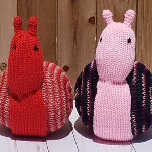 Puede incluir: Dos juguetes de caracol de punto, uno rojo con rayas blancas y otro rosa con rayas negras y burdeos.