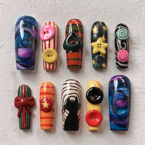 May include: A collection of ten uniquely designed nail art pieces. Each nail features a different design, including swirls, stripes, buttons, a star, a bow, and a cat silhouette. The color palette includes blue, pink, yellow, red, green, and black.