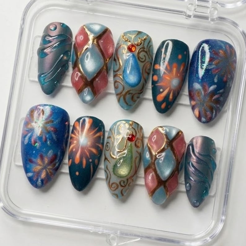 May include: A set of ten artificial nails in a clear plastic case. The nails feature various designs, including abstract swirls, geometric patterns, and firework-like bursts. Colors include teal, pink, gold, and blue, with a glossy finish.
