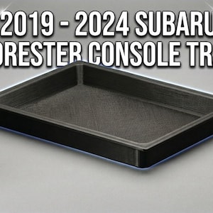 Puede incluir: Una bandeja de consola negra para vehículos Subaru Forester 2019-2024. La bandeja es rectangular con una superficie texturizada y bordes elevados. El texto en la imagen dice "2019-2024 SUBARU FORESTER CONSOLE TRAY."