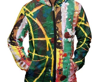 Puede incluir: Una chaqueta cortavientos con capucha y cremallera que presenta un patrón abstracto de salpicaduras de pintura en tonos vibrantes de verde, amarillo, rojo y blanco. La prenda ligera incluye una cremallera frontal negra y dos bolsillos.
