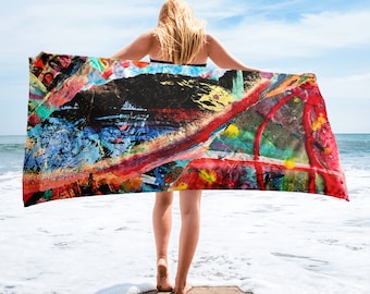 May include: A colourful beach towel with an abstract paint splatter design in shades of red, blue, yellow, green, and black. The towel is being held by a person on a beach.